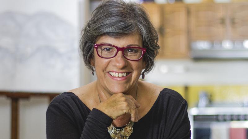 Photo of filmmaker Luisa de la Ville looking into the camera and smiling. They have short, graying hair and red glasses.
