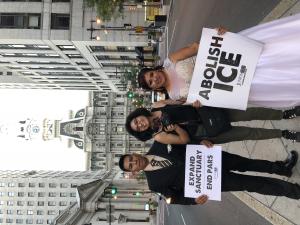 Man and woman in wedding outfits holding "Abolish ICE" posters standing to each side of the director